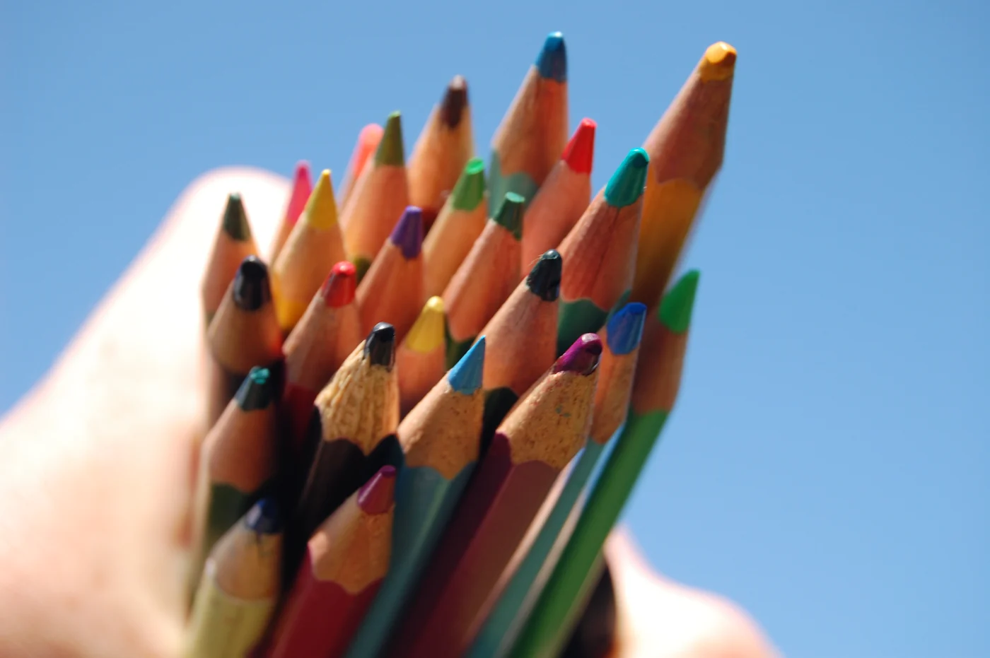 A hand holding a bundle of coloured pencils against a blue sky